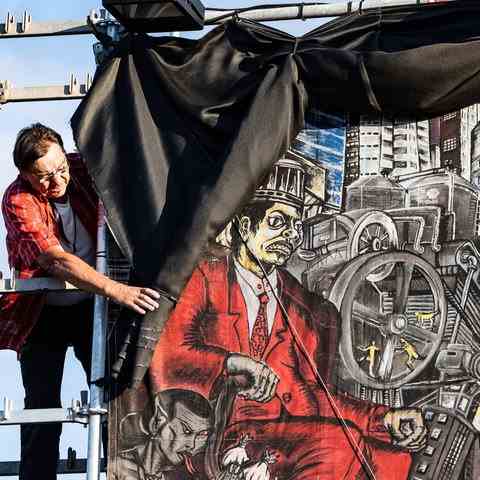 A worker stands at the top of a scaffold and rolls black fabric over a large-format, very small-scale colored image.