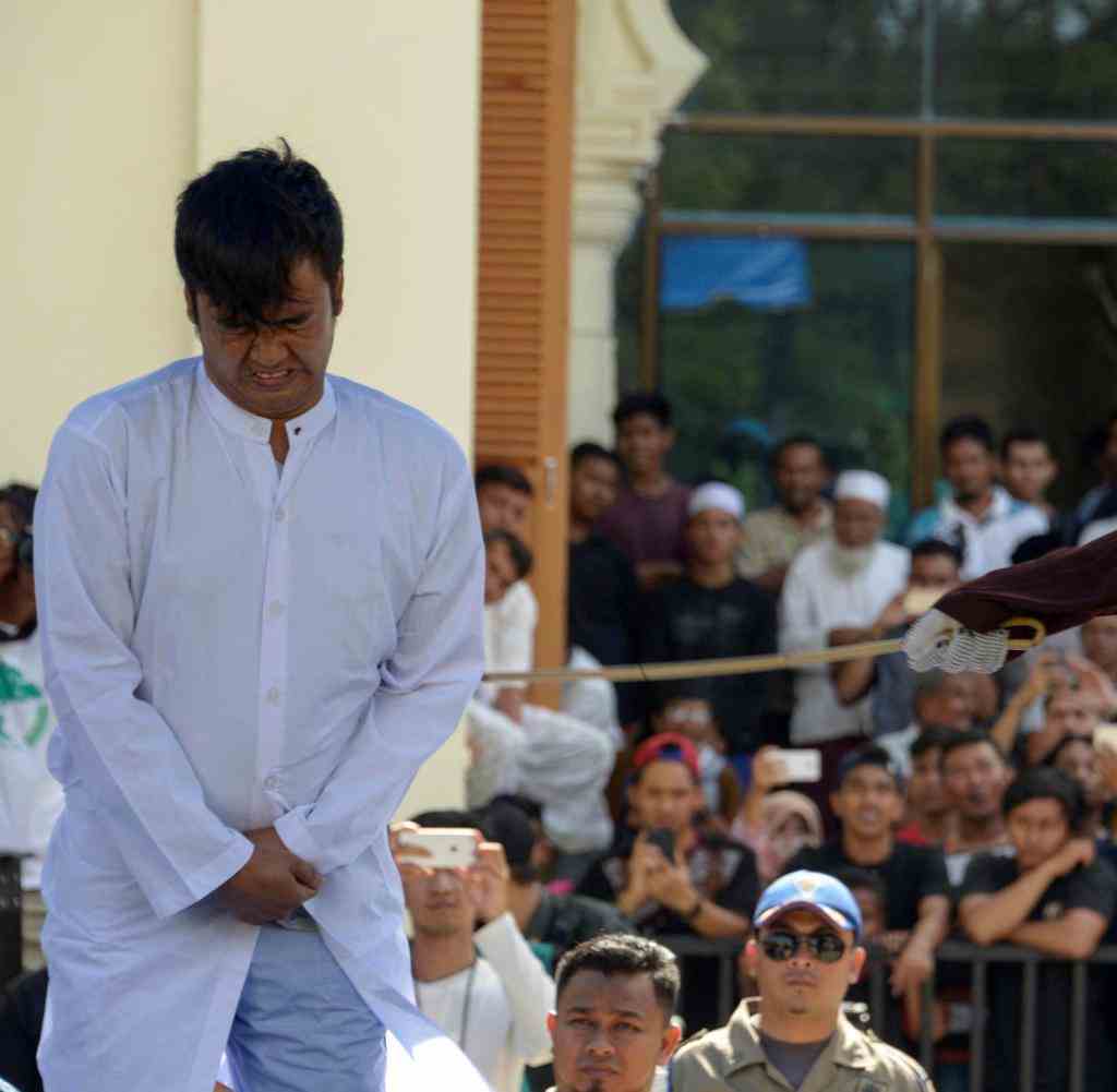 EDITORS NOTE: Graphic content / A member of Indonesia's Sharia police (R) whips a man (L) accused of having gay sex during a public caning ceremony outside a mosque in Banda Aceh, capital of Aceh province on July 13, 2018. - A Gay couple was publicly whipped in Indonesia's conservative Aceh province on July 13, despite an earlier pledge by officials to stop the punishment after it drew international criticism.  (Photo by CHAIDEER MAHYUDDIN / AFP)