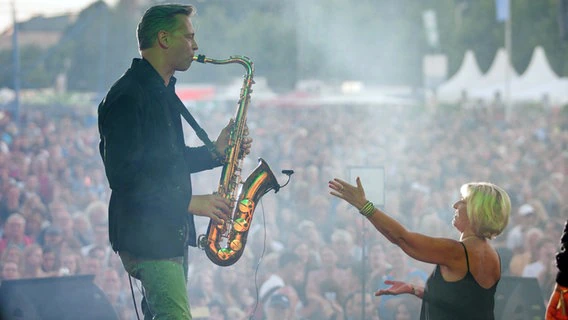 Hanne Pries, singer of the band Tiffany, points to the band's saxophonist: Joachim Kopp during a concert on the NDR stage at Ostseekai at Kiel Week.  © NDR Photo: Björn Schaller