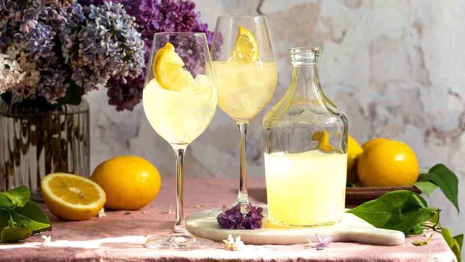 A bottle of Italian traditional liqueur Limoncello with glasses, lemons and a vase with blooming lilacs