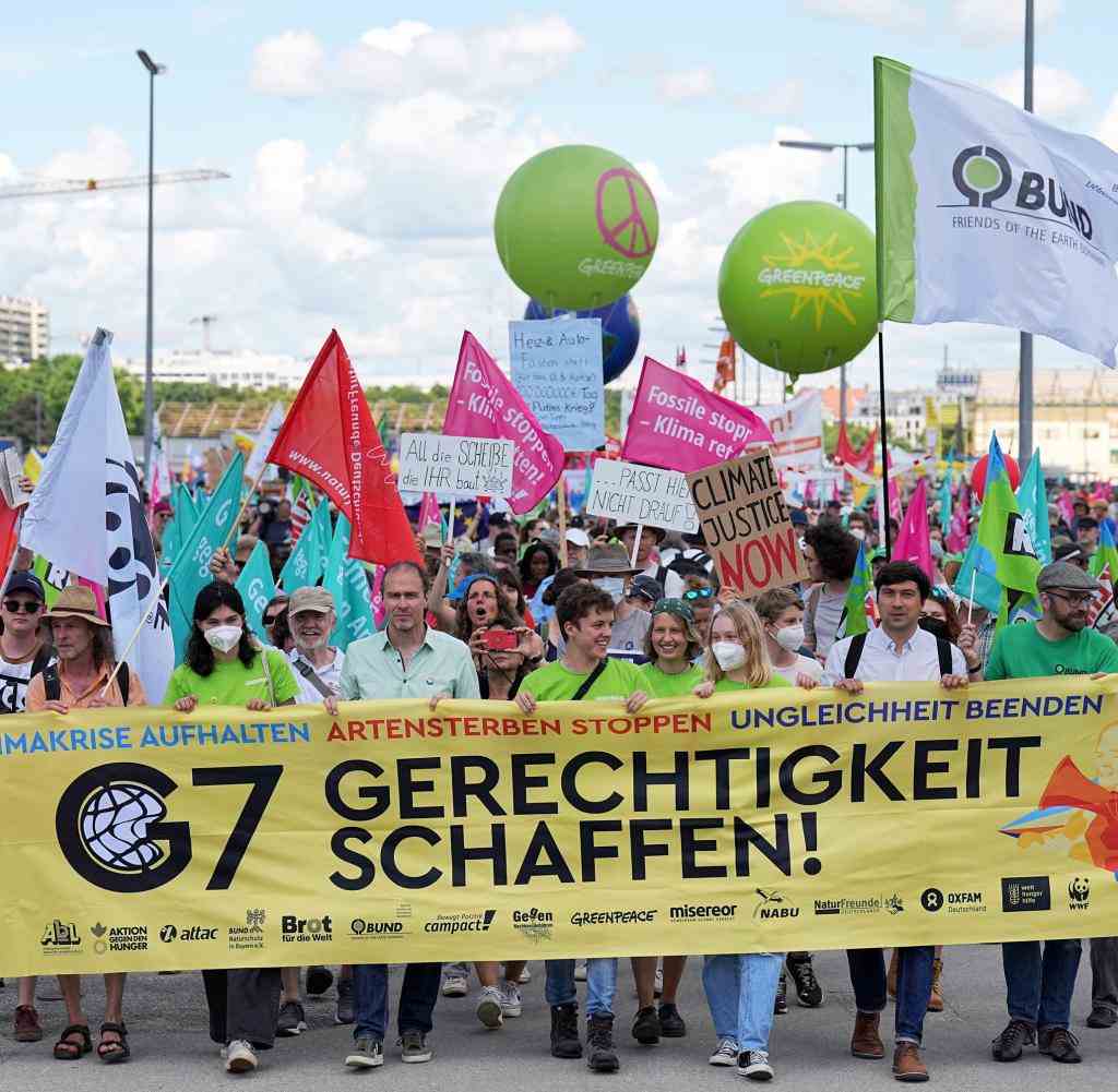 Teilnehmer einer Demonstration für einen besseren Klima- und Artenschutz und gegen Hunger und Armut halten ein Banner mit der Aufschrift „G 7 Gerechtigkeit schaffen“
