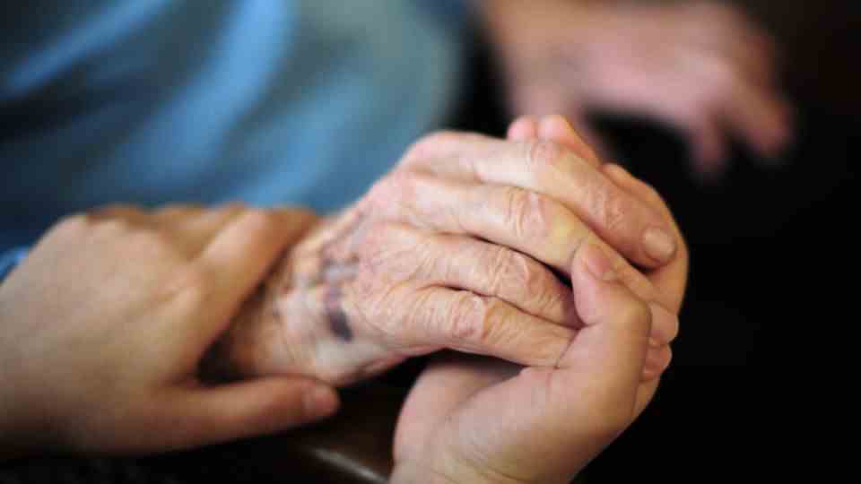 The hand of a nurse rests on the hand of a resident of the retirement home