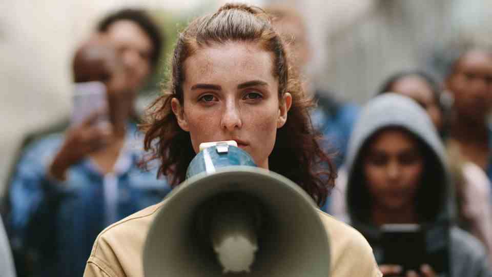 A young Generation Z woman stands on the street with a megaphone.