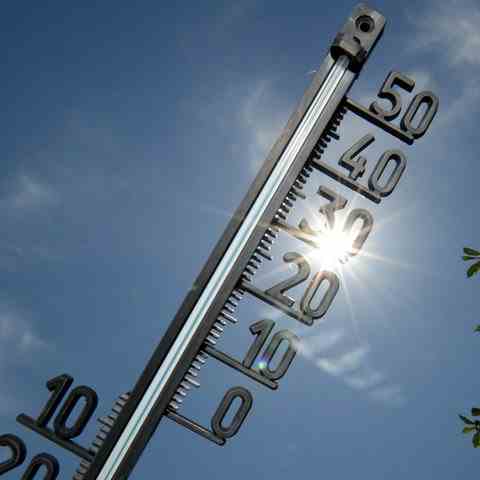 A thermometer can be seen against a bright blue sky with glaring sunlight.