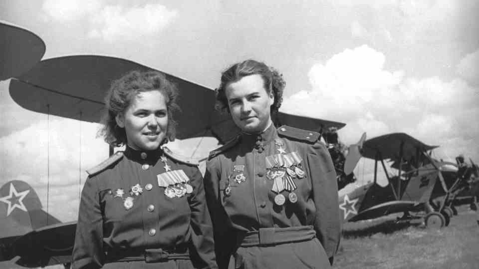 Two decorated female pilots in front of their biplanes.