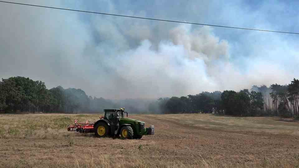A tractor stands on a field near Gransee on Monday while clouds of smoke rise from the forest