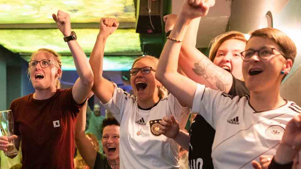 Soccer fans follow the game in a pub and cheer the goal of the German team