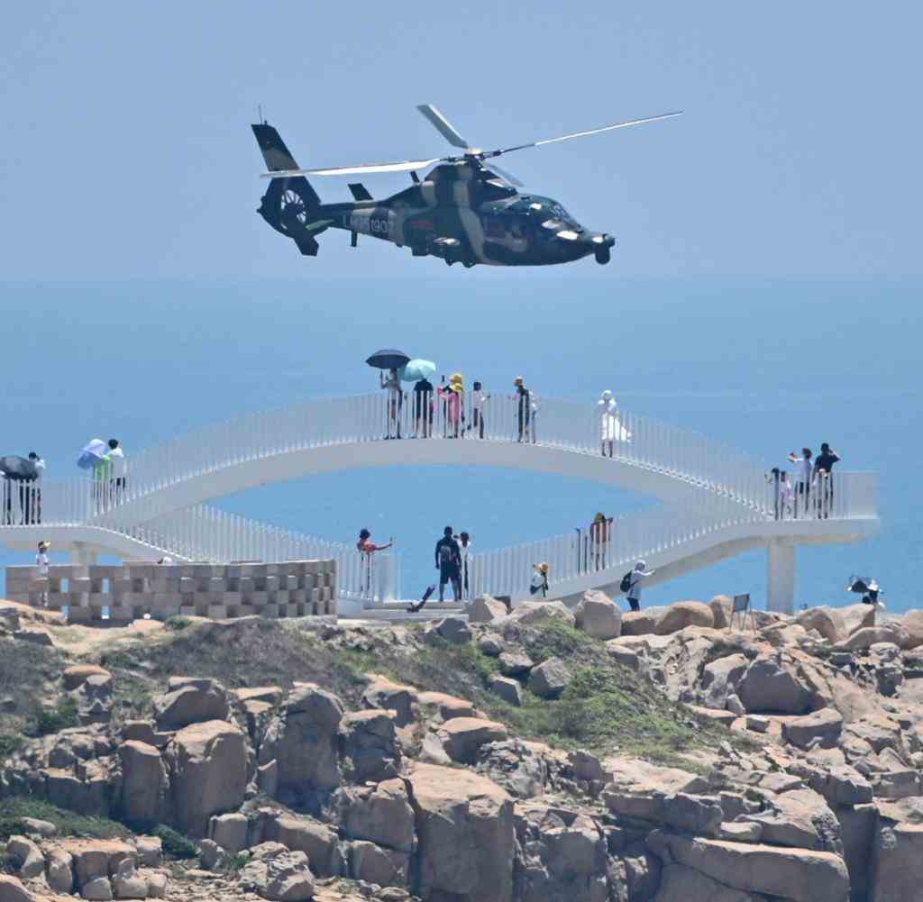 TOPSHOT - Tourists look on as a Chinese military helicopter flies past Pingtan island, one of mainland China's closest point from Taiwan, in Fujian province on August 4, 2022, ahead of massive military drills off Taiwan following US House Speaker Nancy Pelosi's visit to the self-ruled island. - China is due on August 4 to kick off its largest-ever military exercises encircling Taiwan, in a show of force straddling vital international shipping lanes following a visit to the self-ruled island by US House Speaker Nancy Pelosi. (Photo by Hector RETAMAL / AFP)