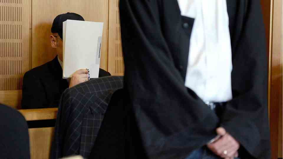 Olaf H. in court.  He covers his face with a file.
