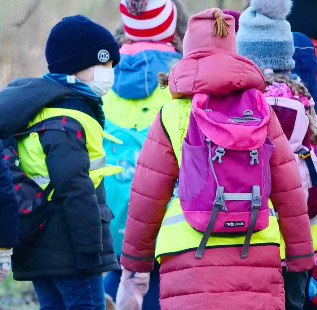 January 28, 2022, Berlin.  First grade students at an elementary school follow their teacher on a class field trip on a January day.  They carry backpacks with provisions and yellow warning vests.  A boy has a mask on his face to protect against the corona virus.  Photo: Wolfram Steinberg/dpa