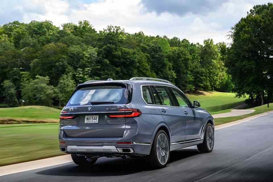 A side rear view of a BMW X7 drives on a road