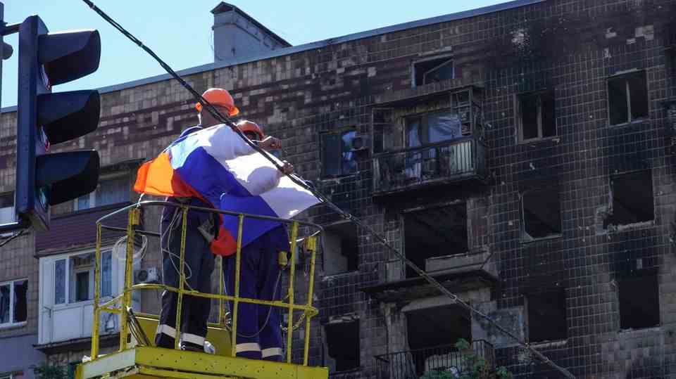 Workers fix a Russian flag over a street in Mariupol