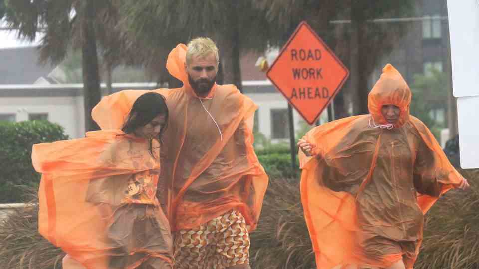 A man and two women in orange raincoats walk down a street in Florida, United States