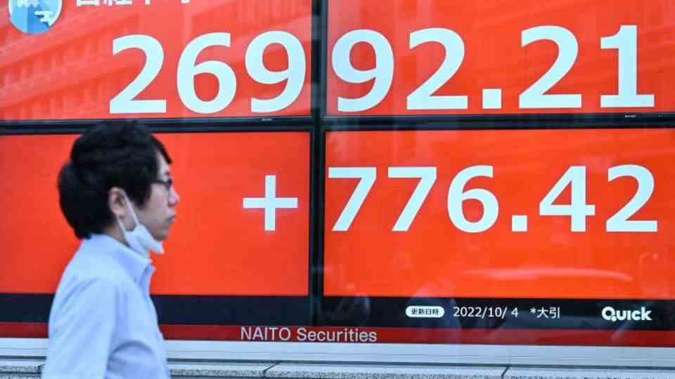 Tokyo, Japan.  A man walks past an electronic scoreboard that announces the close of the stock market in white digits on red.  Share prices also rose in the Japanese capital after Wall Street stocks recovered, amid fears of a recession.