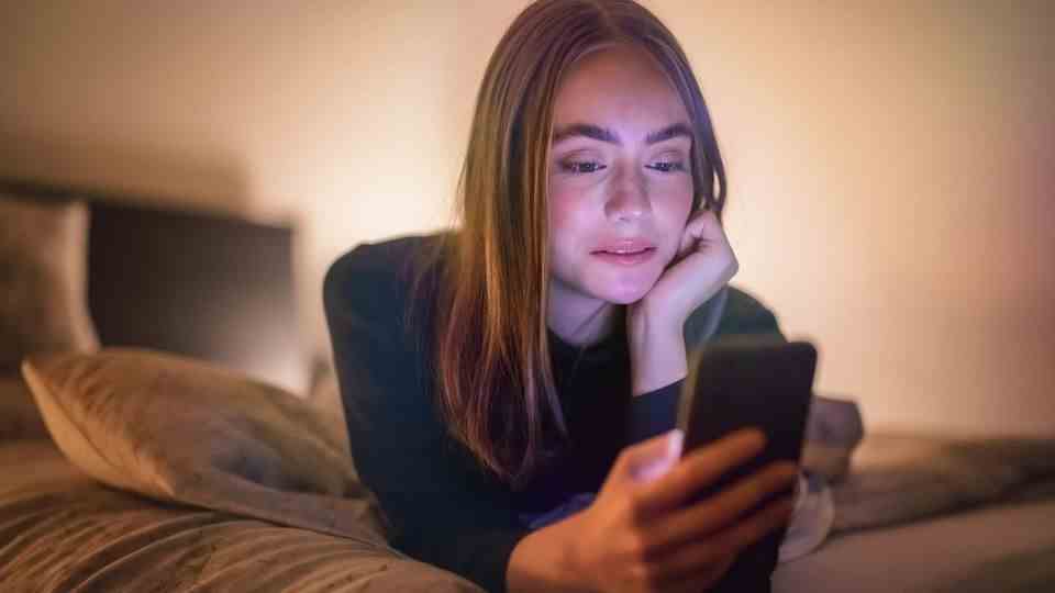 A young woman lies in bed and looks at her smartphone