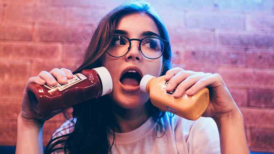 Healthy eating: young woman holds two bottles of ketchup in front of her mouth