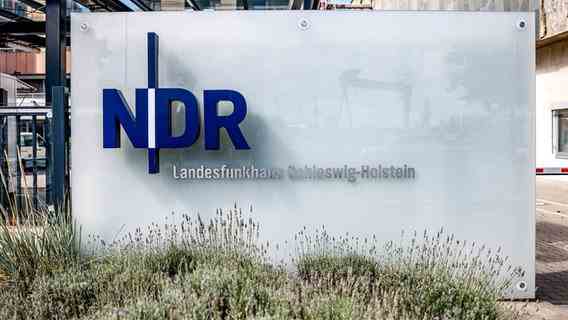 The NDR logo is attached to a glass plate at the entrance to the Landesfunkhaus Schleswig-Holstein.  © dpa Photo: Axel Heimken