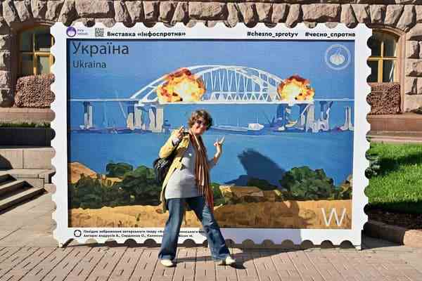 Une femme pose devant un grand timbre représentant l'explosion sur le pont de Crimée installé à Kiev le 8 octobre 2022. 