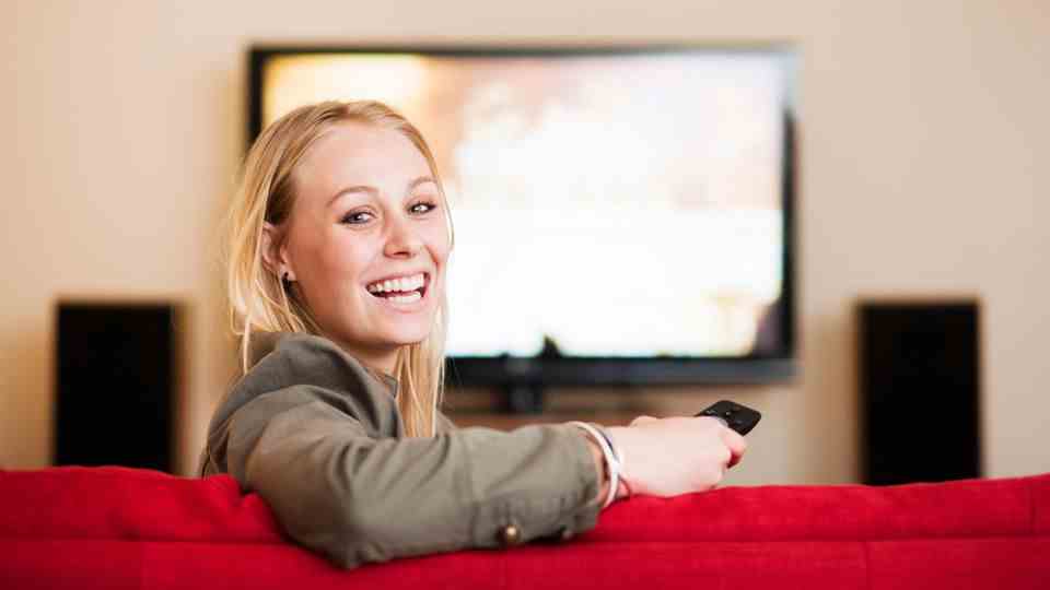 A woman sits in front of the television and looks happily into the camera