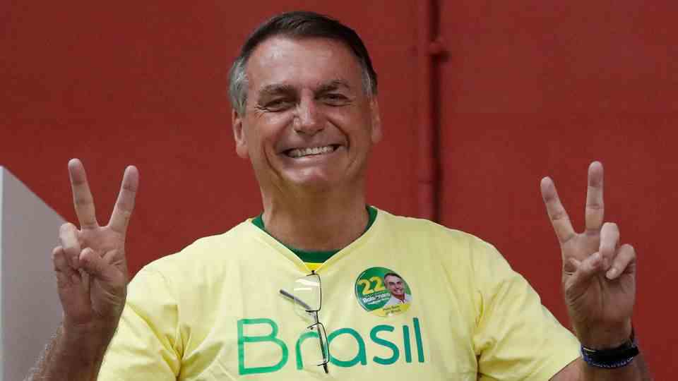 A tanned elderly man in yellow "Brazil"-T-Shirt makes victory signs with both hands and smiles broadly
