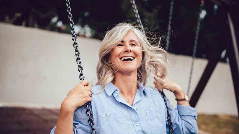 An elderly woman sits on a swing and laughs.
