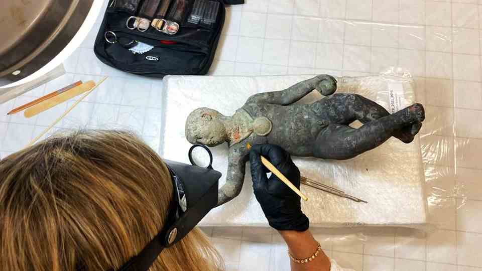Researcher examines bronze figure depicting a child
