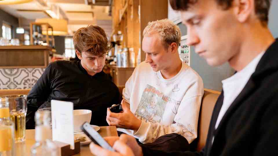 Drei junge Männer sitzen an einem Tisch und schauen auf ihre Handys