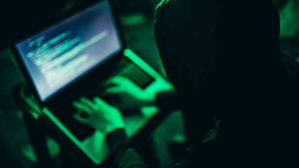 A hacker in a dark hoodie at a laptop
