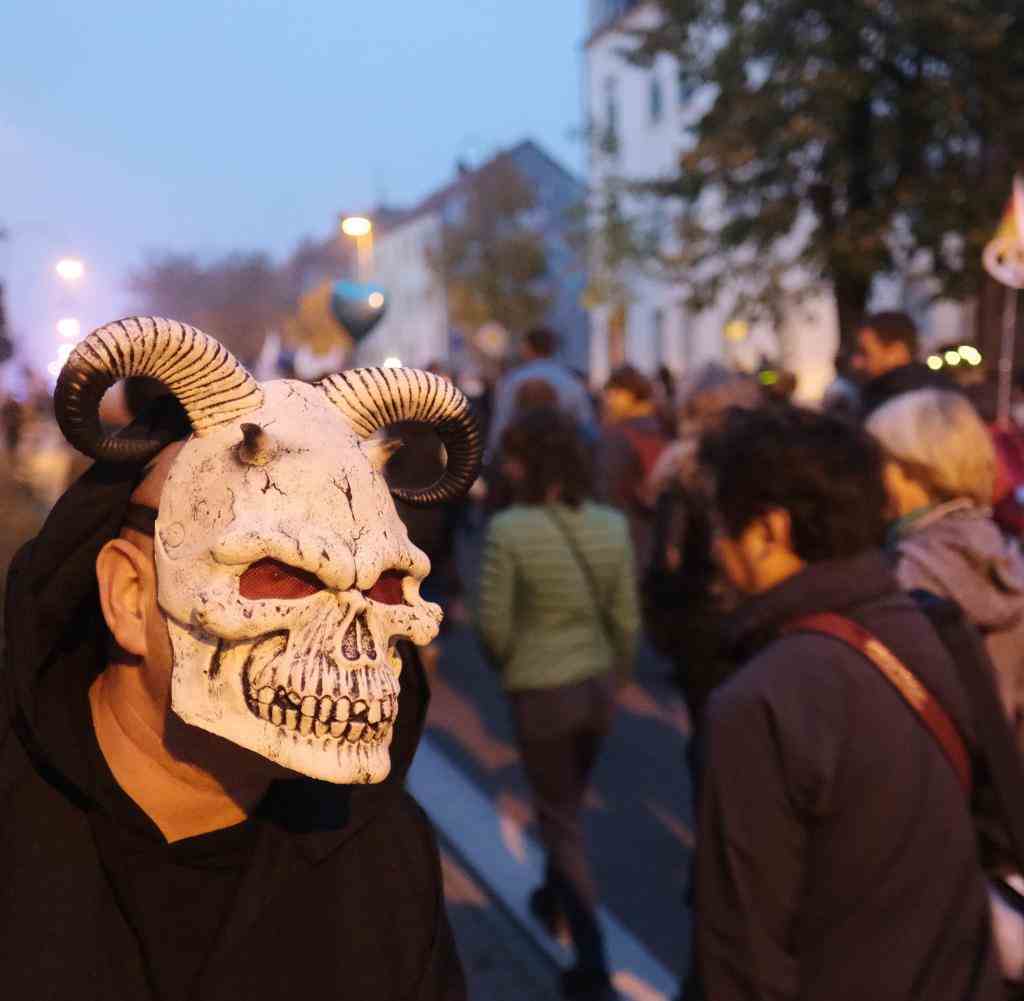 Demonstrators walk down a street in Wittenberg while a passer-by in Halloween costume looks on