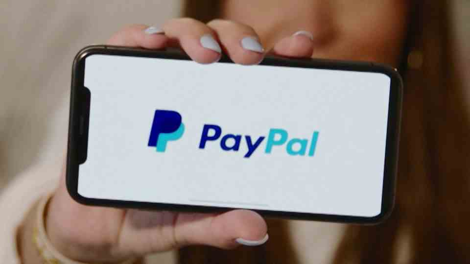 A woman is holding her smartphone with the "PayPal"-Logo in front of the camera.
