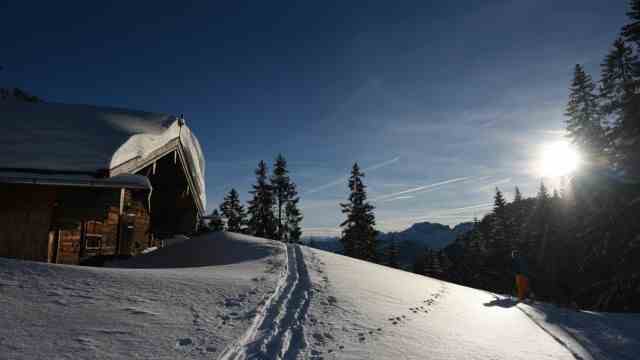 Leisure time in Bavaria: Two snowshoe hikers walk past a snow-covered mountain hut on Spitzingsee.