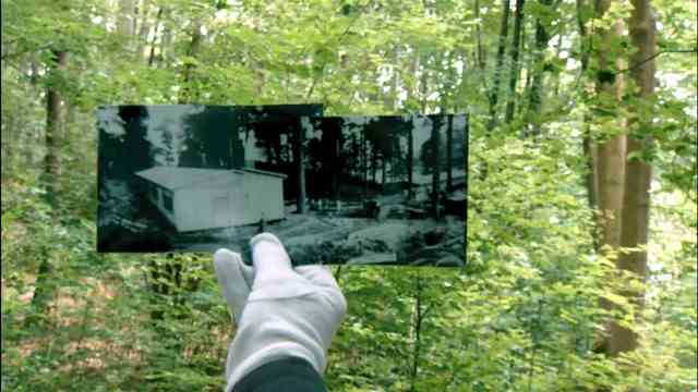 3sat documentation: Picture in picture: The old motif of a concentration camp barracks can no longer be seen under the overgrown trees.