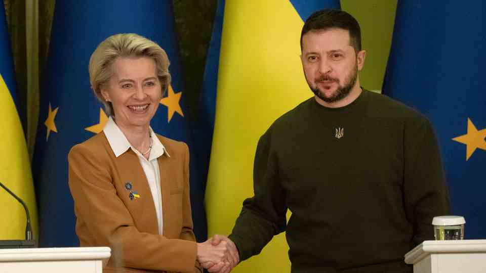Ursula von der Leyen and Volodymyr Zelenskyj shake hands in front of EU and Ukrainian flags