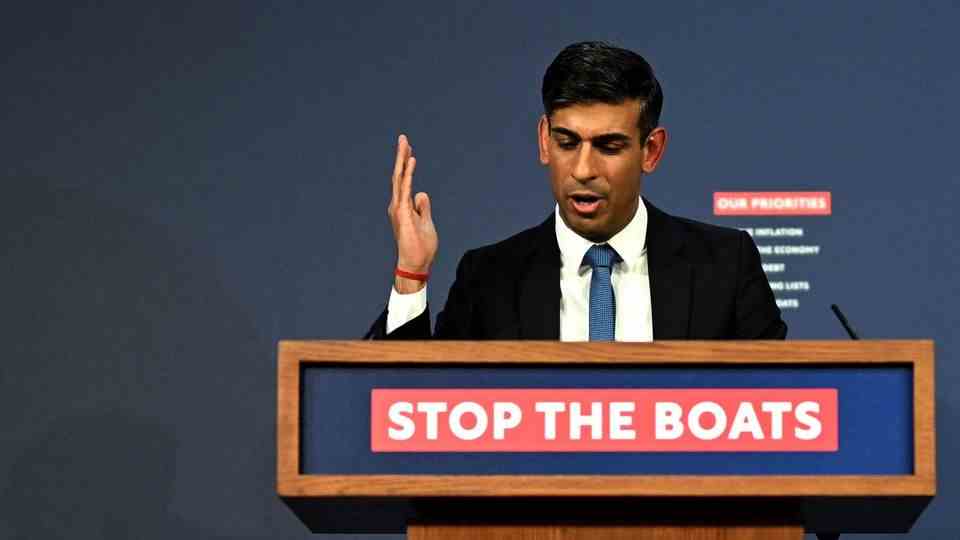 Rishi Sunak, British Prime Minister, speaks at a lectern "Stop the boats"-Lettering