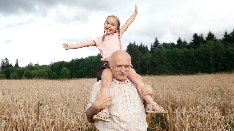 An elderly man carries a girl on his shoulders