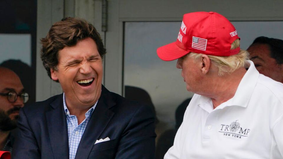 Fox News presenter Tucker Carlson laughs alongside ex-US President Donald Trump