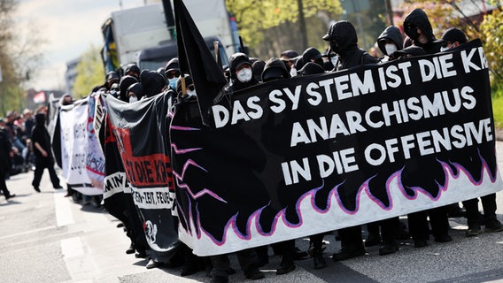 Participants in a May Day demonstration under the motto "The system is the crisis, anarchism on the offensive!" stand with banners and predominantly black clothing at the Hagenbeck Zoo in Hamburg.  © picture alliance/dpa Photo: Christian Charisius