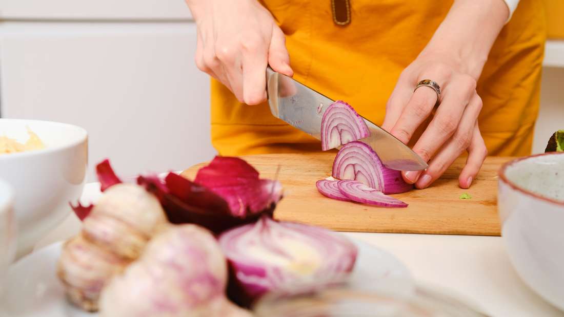 A woman cuts red onions.