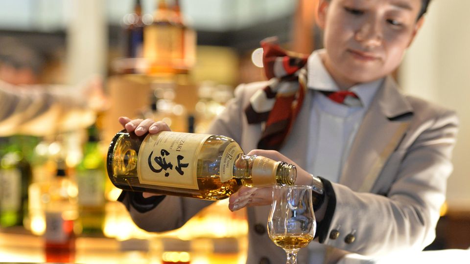 A barmaid pours whiskey from a Yamazaki bottle
