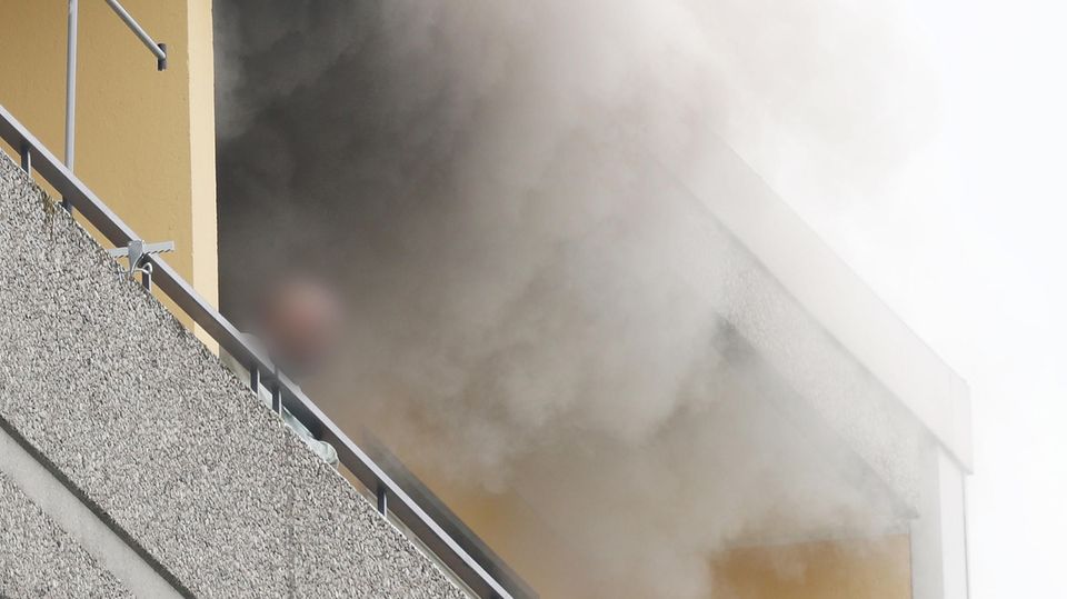 A person stands on the balcony of a high-rise building with smoke billowing out