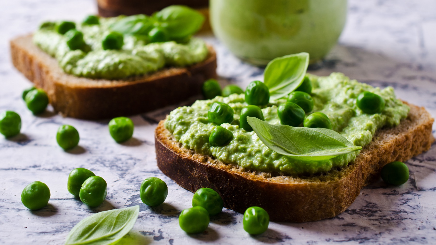 Two toasts with the basil and pea cream on a gray background.