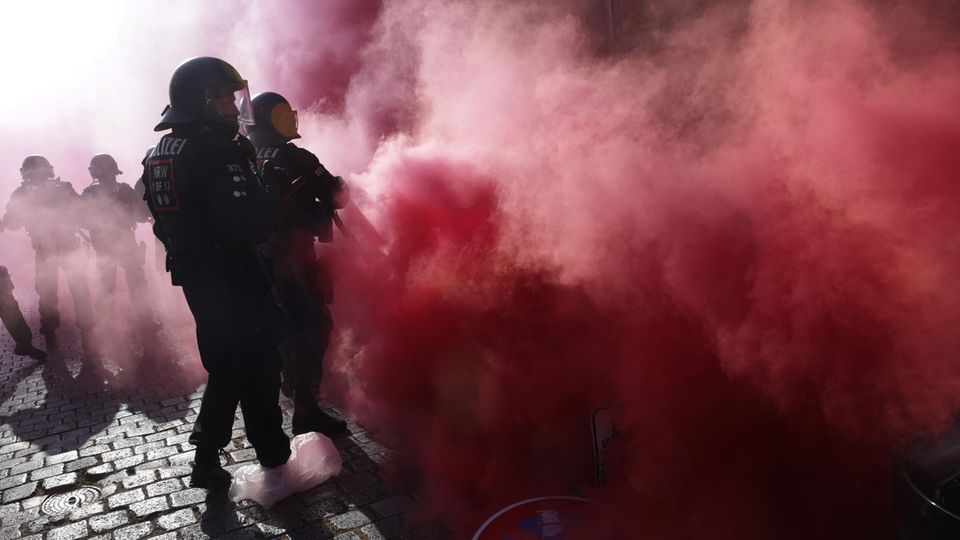 On Day X in Leipzig, helmeted police officers are enveloped in red smoke