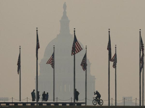 Tourists walk around the base of the Washington Monument as smoke from a wildfire blankets the US Capitol on the National Mall in Washington, DC.