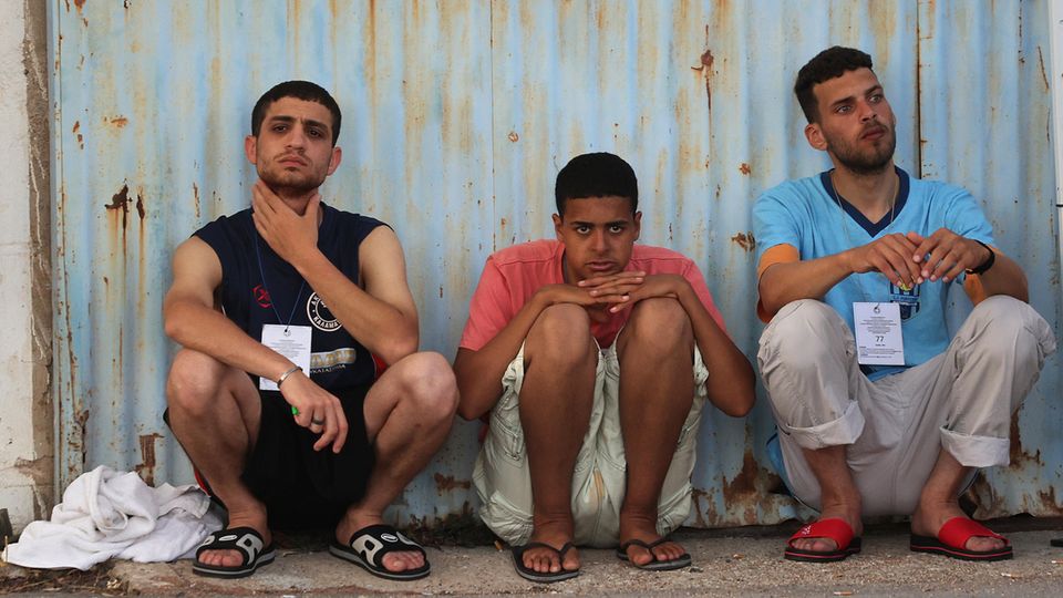 Three men crouch side by side on the floor.  They are survivors of the boat accident in Greece