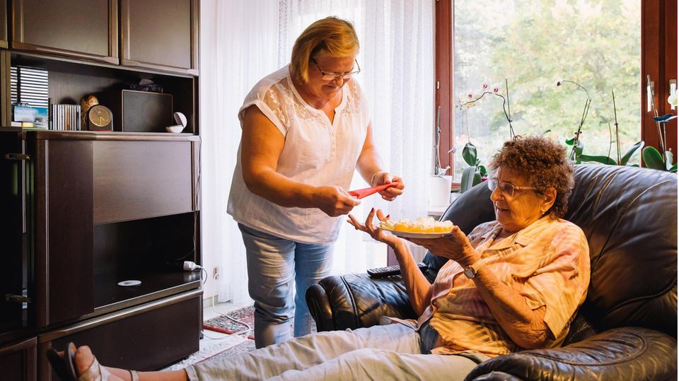 Nurse Małgorzata K. hands the elderly Brigitte M., who is sitting on a recliner, a napkin