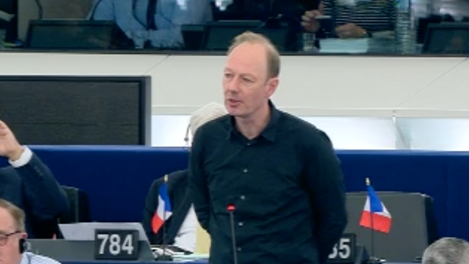 Satirist MArtin Sonneborn stands in front of a microphone at his seat in the EU Parliament and speaks