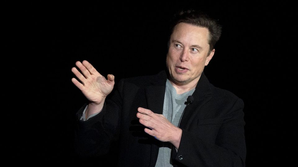 Elon Musk points to the right with both hands and looks in the direction with wide eyes