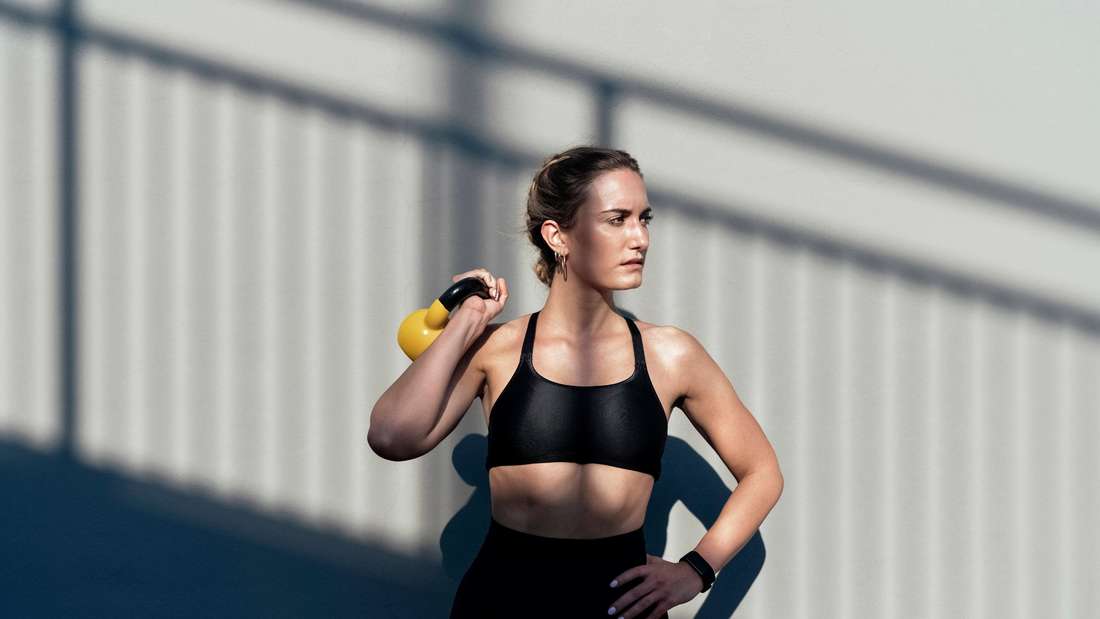 Young woman has a training device, the so-called kettlebell, in her hand. 