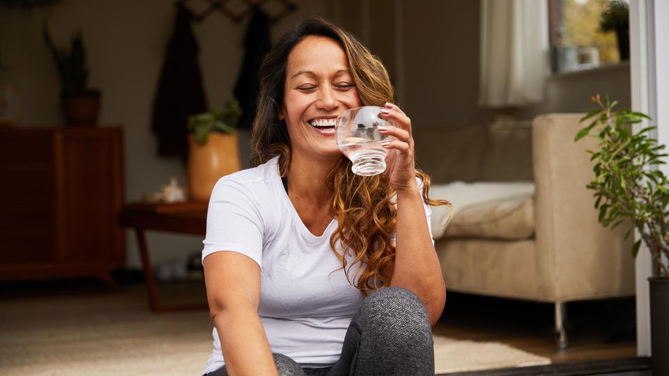 Drinking water in summer: A woman holds a glass of water in her hand and laughs