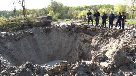 Ordnance clearance personnel are standing at a crater.  © North West Media TV 